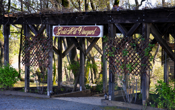 A timber arbor hung with a painted sign reading Gold Hill Vineyard